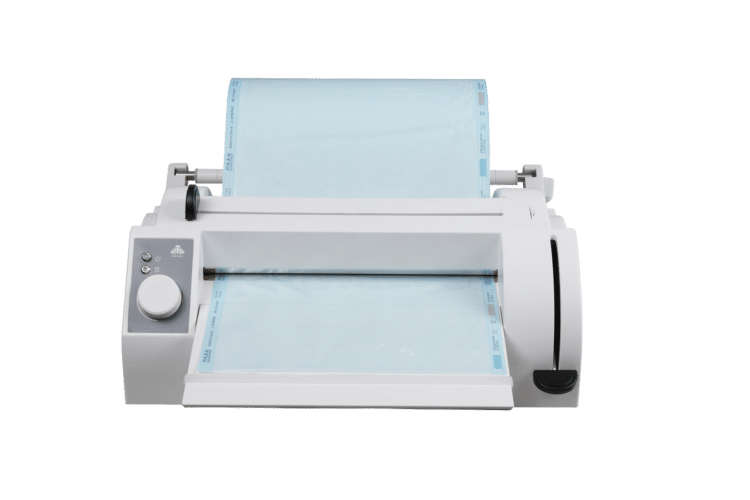 Vue de face d’une soudeuse thermique vétérinaire Pearl Shell Sealer chargée d’un large rouleau de gaine de stérilisation bleu clair, qui passe dans la fente de soudure et ressort sur le plateau avant ; panneau de commande gris à gauche, levier noir à droite.