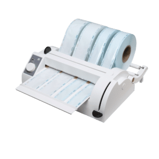 Vue en trois quarts d’une soudeuse thermique vétérinaire Pearl Shell Sealer blanche, avec quatre rouleaux de gaines de stérilisation de largeurs différentes montés sur les tiges à l’arrière, et plusieurs bandes de gaine découpées posées sur le plateau avant ; panneau gris et molette à gauche, levier noir à droite.